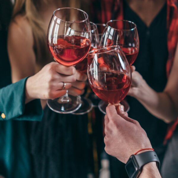 Personas brindando con copas de vino rosado.