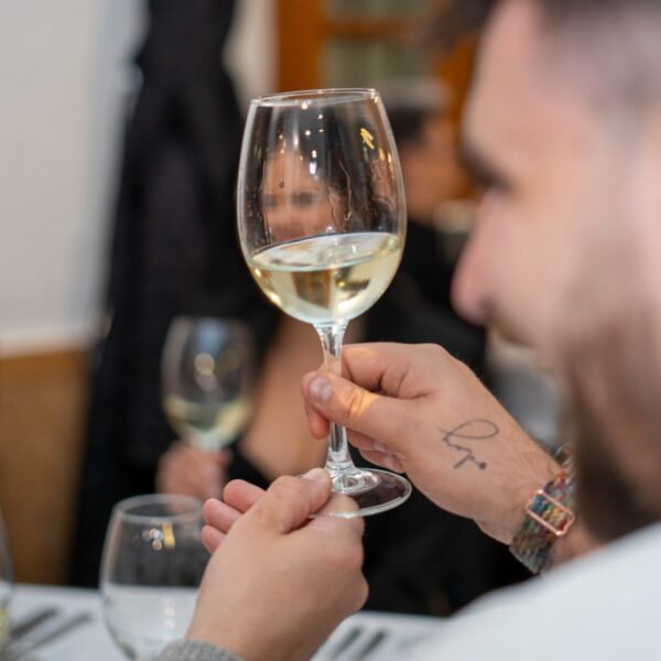 Hombre degustando vino blanco en evento social.